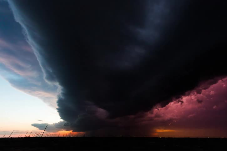 Storm clouds with rapid flashes of lightening form over rural farmland blackening the sky