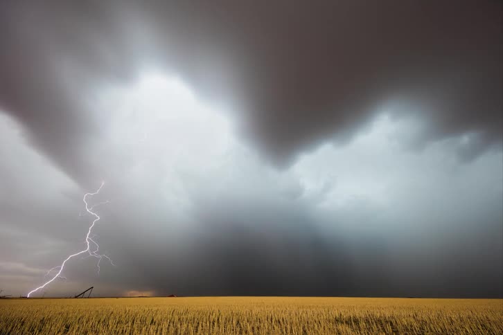 Storm clouds move over farmland as rain pours down and lightning strikes