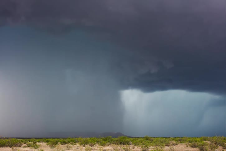 Dark storm clouds move across the sky as rain pours on the land as an automobile passes by