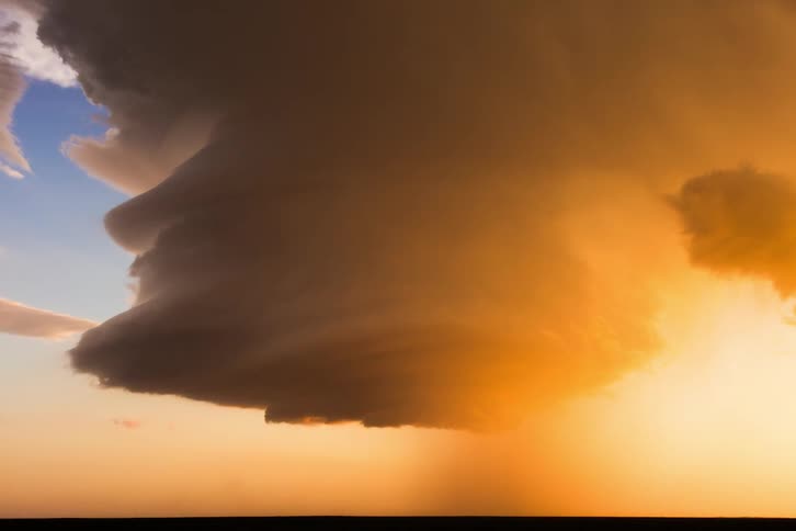 Storm clouds twist and turn and pour down rain as the sun shines brightly on the horizon