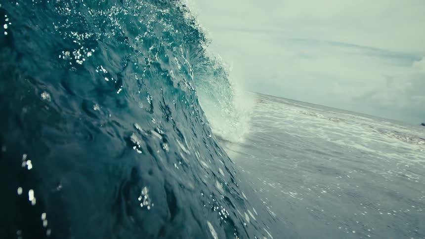 Wave rolling toward beach crashes just above seafloor on a cloudy day