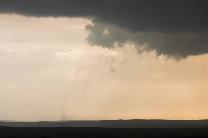 A tornado funnel cloud moves over the land and up into storm clouds