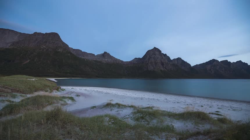 Landscape of sandy beach near the water with mountain range in the background