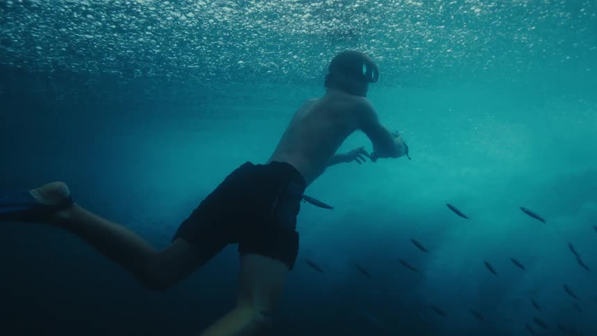 A diver with a camera films the underside of a wave