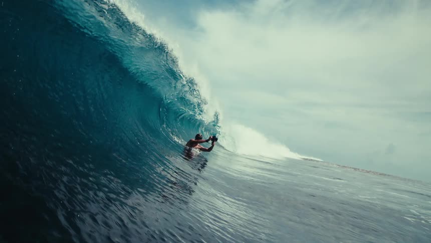 A huge blue wave breaks over a sinking man and the wave is seen from below the water