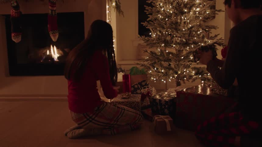 Boy and girl knelt on the floor smiling while checking the christmas gifts at night