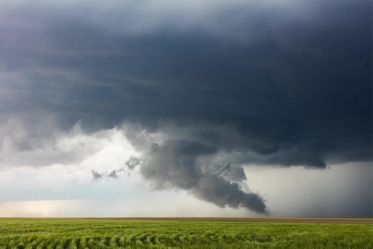 Dark storm clouds start forming a tornado over a farm field