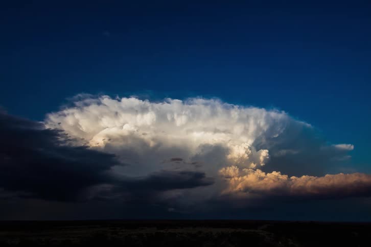 Dark storm clouds move in under cumulus clouds pouring rain on the ground as the sky grows dark