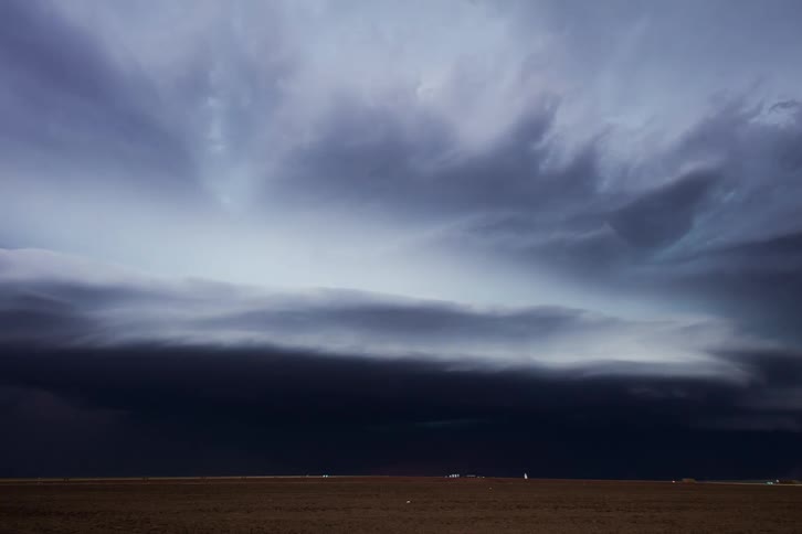 Dark storm clouds move across the land as lightning flashes and an automobile travels on the road