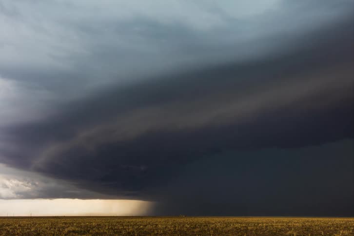 A dark supercell storm pours rain and moves across the land as lightning flashes