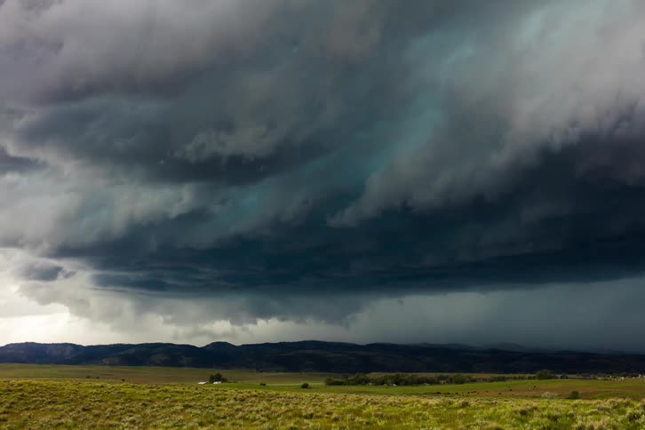 Storm clouds rolling over a grassy rural farmland and covering mountains in the background