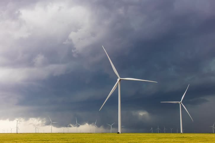 Turbines on a wind farm spin as storm clouds move across the sky