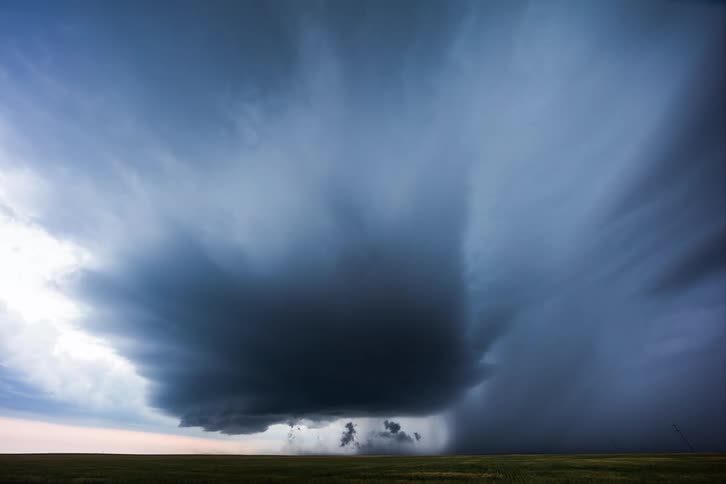 Lighting flashes as a supercell storm moves in rotation low over the land and pours rain as traffic moves on the road
