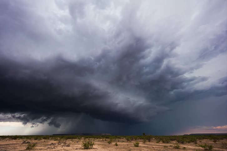 A supercell storm pours rain on the land as it moves across the sky