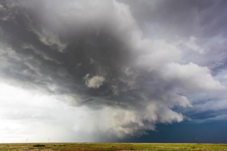 Storm clouds roll in and out over a flat grassland prairie