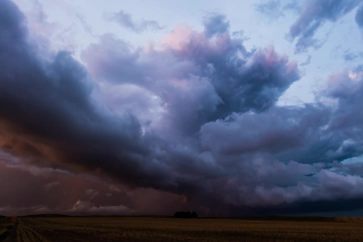 Storm clouds move over farmland in a darkening sky as lightning flashes