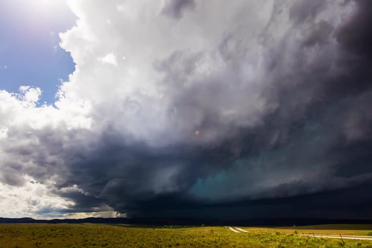 Blue sky is covered by a large rain cloud over a flat terrain