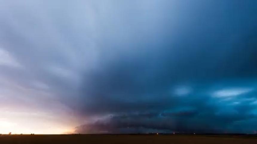 Dark storm clouds move across the land as lightning flashes and an automobile travels on the road