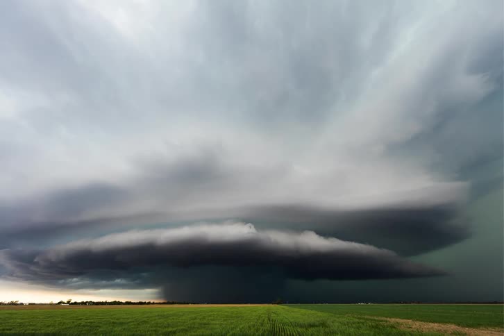 A storm of clouds forming in the sky and with some lightning falling over a green field