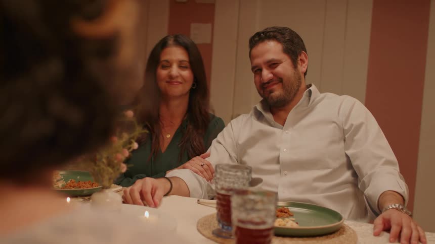 A couple sitting at a table look at each other and smile and then look at someone in front of them