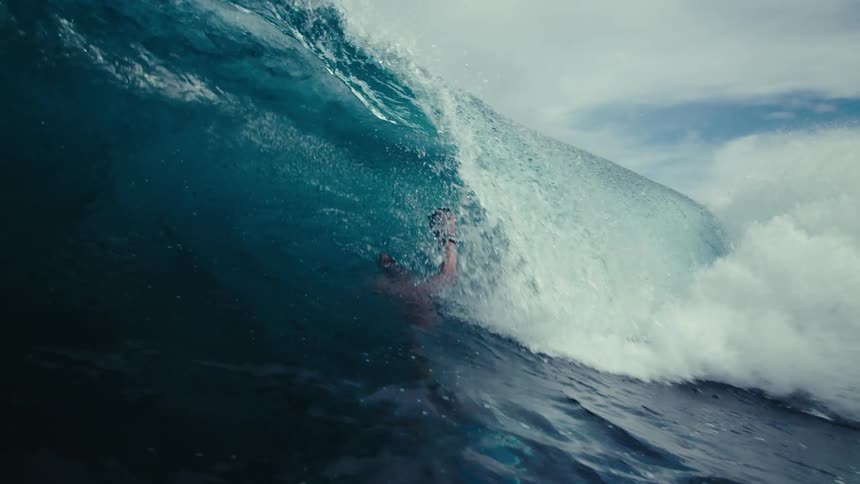A man swimming with a camera filming a wave coming towards him that then pushes him underwater