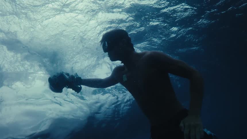 A man with a camera in an underwater scene with light rays penetrating through the clear water