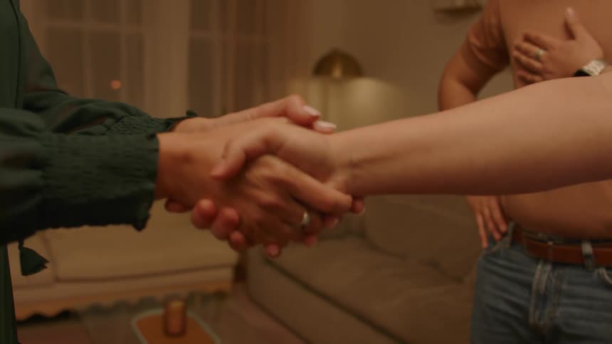 Friends shake hands while standing in living room at night