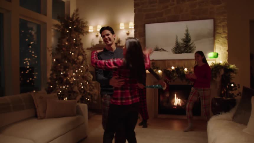 Four people two adults and two teenagers dance in a living room