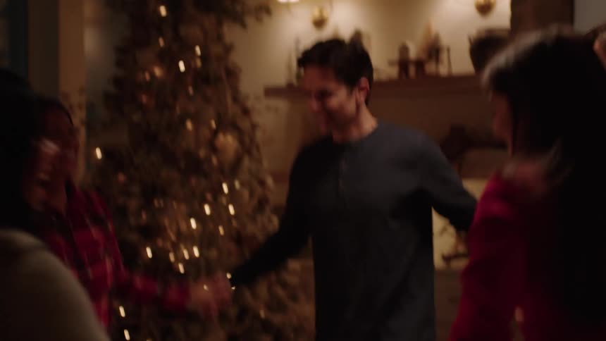 Some people are in a living room with christmas decorations and they are all holding hands spinning and dancing