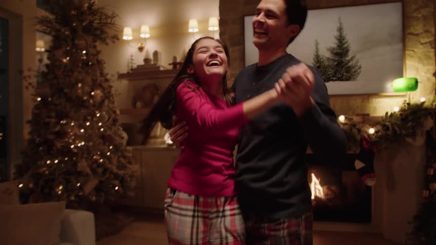 A little girl and her dad are dancing in a room and family is cheering during Christmas