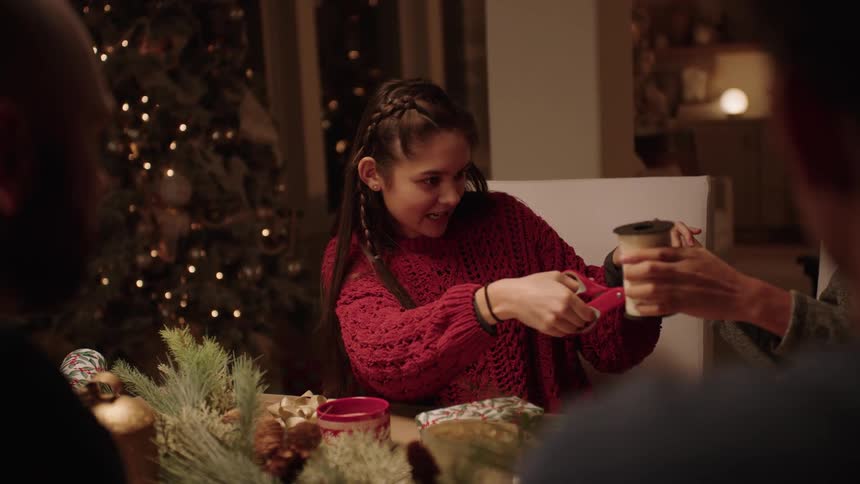 A young girl cutting a ribbon to wrap Christmas presents with her family