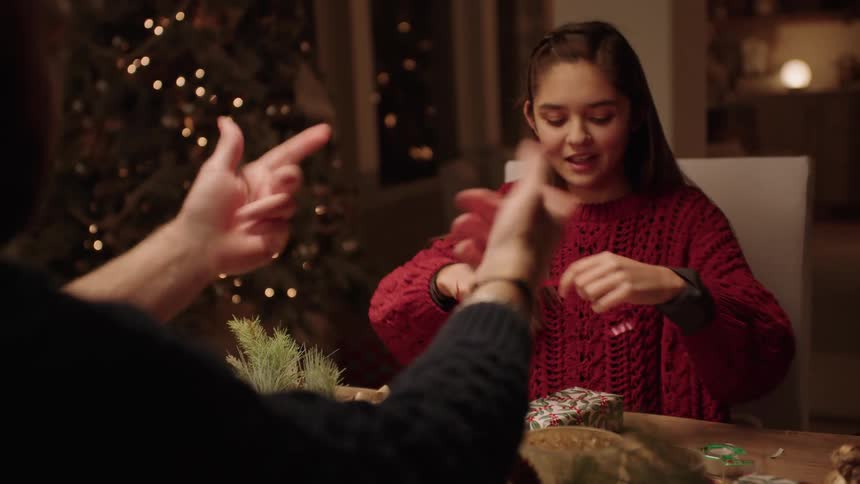 Adults and children sitting at a table with the girl tying a gift ribbon