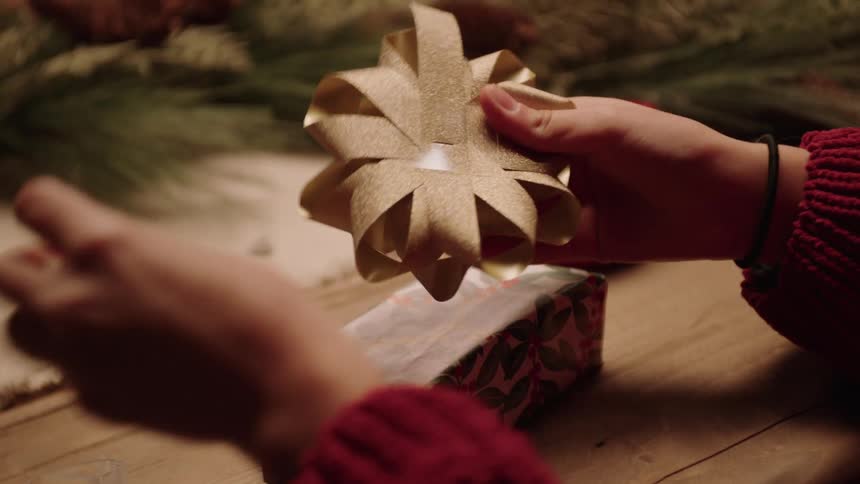 Girl puts a large golden bow on a christmas present she is wrapping