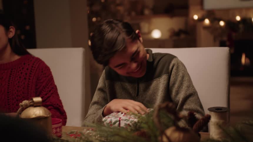 Boy laughs while opening a christmas present at the table