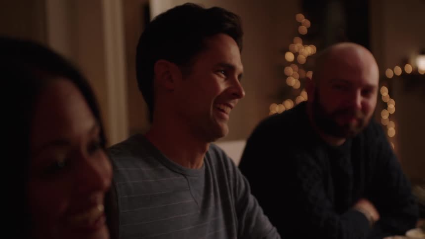 A man is sitting next to another man and they are talking to a woman and then looks straight ahead and everyone is smiling