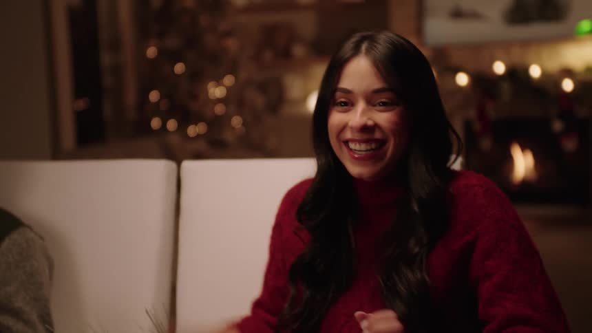 Smiling and laughing woman talks while at dinner party in room decorated for christmas