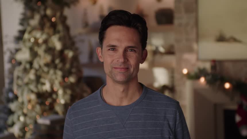 A man standing in a living room with Christmas decorations smiling