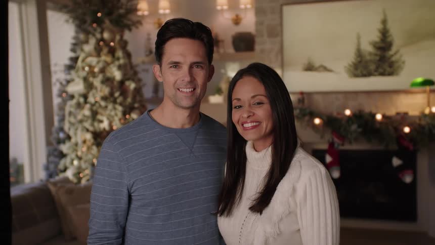 Husband and wife stands in front of christmas tree smiling