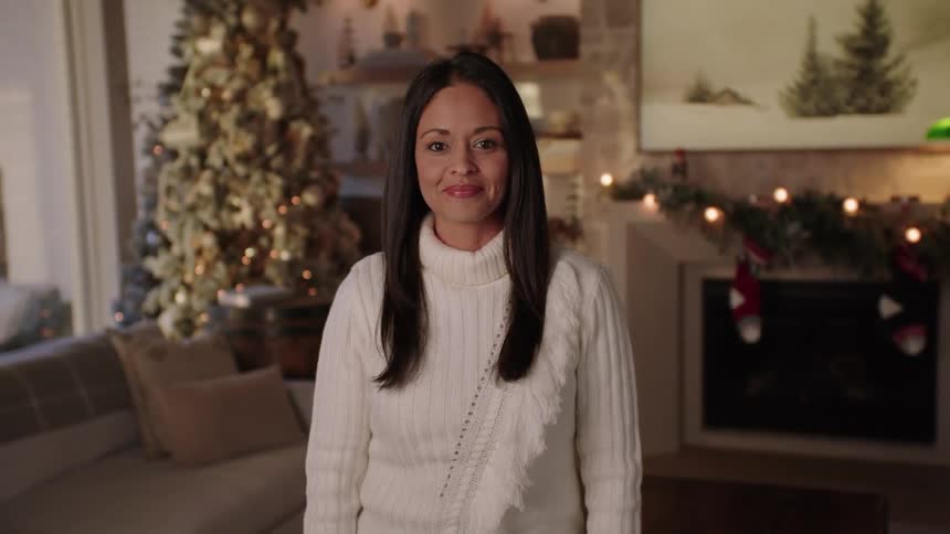 A woman stands in her seasonally decorated living room smiling at the camera