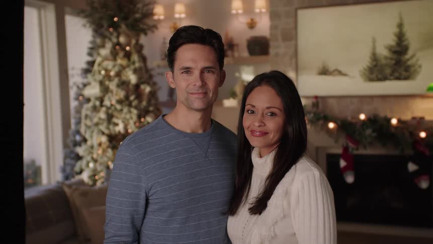 A couple is posing looking forward and with a slight smile and behind them is a christmas decoration