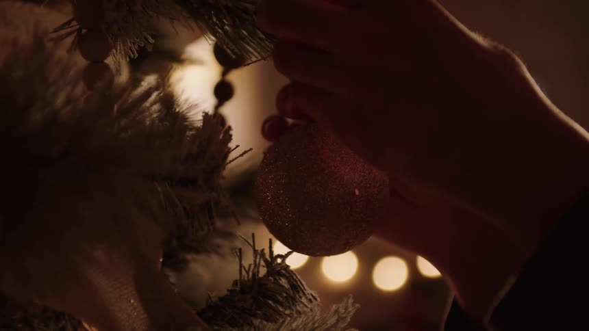 A person hangs an ornament on a christmas tree