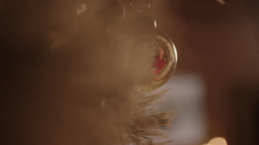Lights and a persons face are seen in the reflection of a christmas ornament