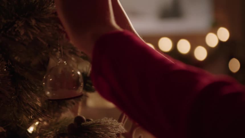 Closeup of a persons hands placing a small globe on a christmas tree