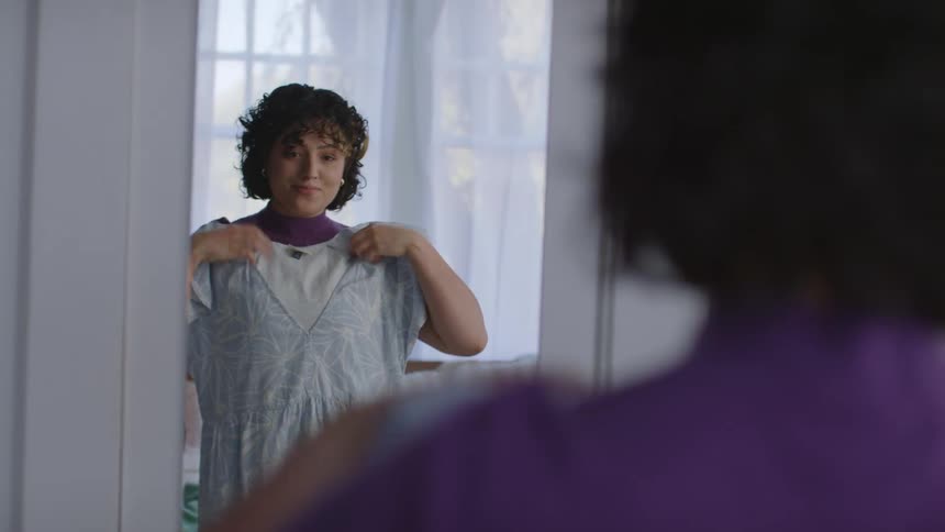Woman wearing purple shirt and jeans tries on clothes in the bedroom