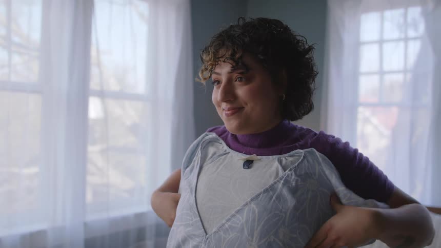 Woman with curly hair and purple shirt tries on shirts in room