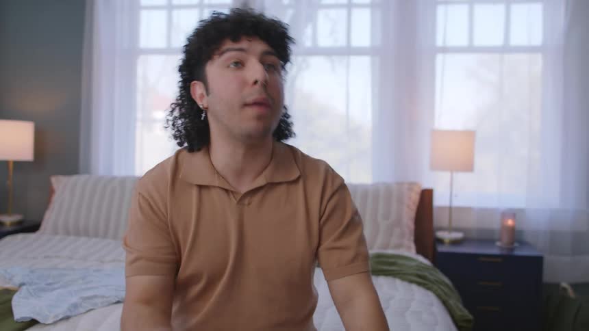 Man sitting on bed in a room during the day talking