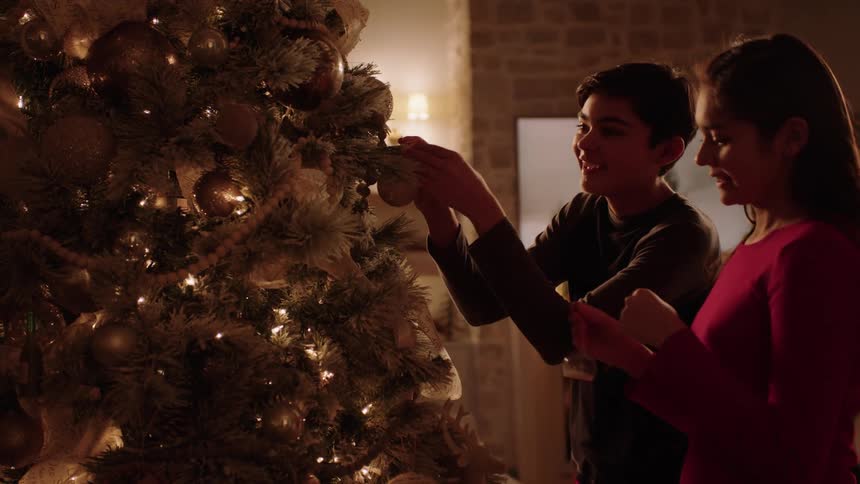 Boy and girl decorates christmas tree with fireplace in the background