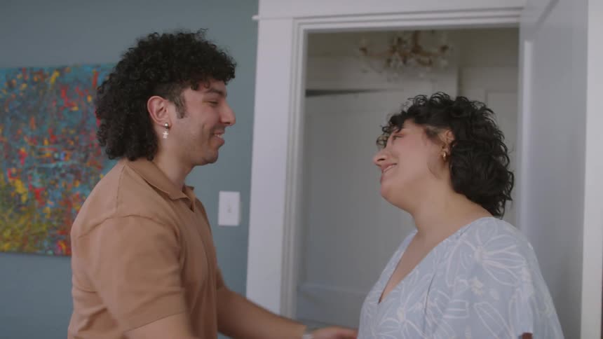 Man stood up from the bed to hold and kiss his wifes hands while they both smile