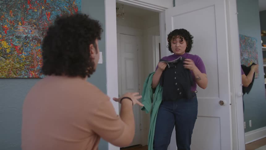 A man sitting in the bedroom helps his partner to choose clothes to wear