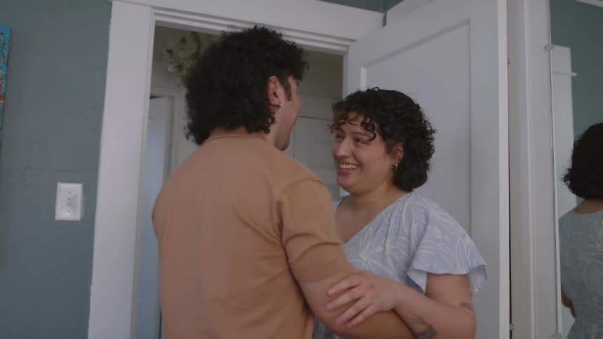 Man waiting in the bedroom hugs his wife complimenting her dress